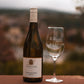 Una botella de vino blanco del tipo Blanc de Noir se encuentra a la izquierda de una copa de vino blanco vacía en una pared de arenisca. 