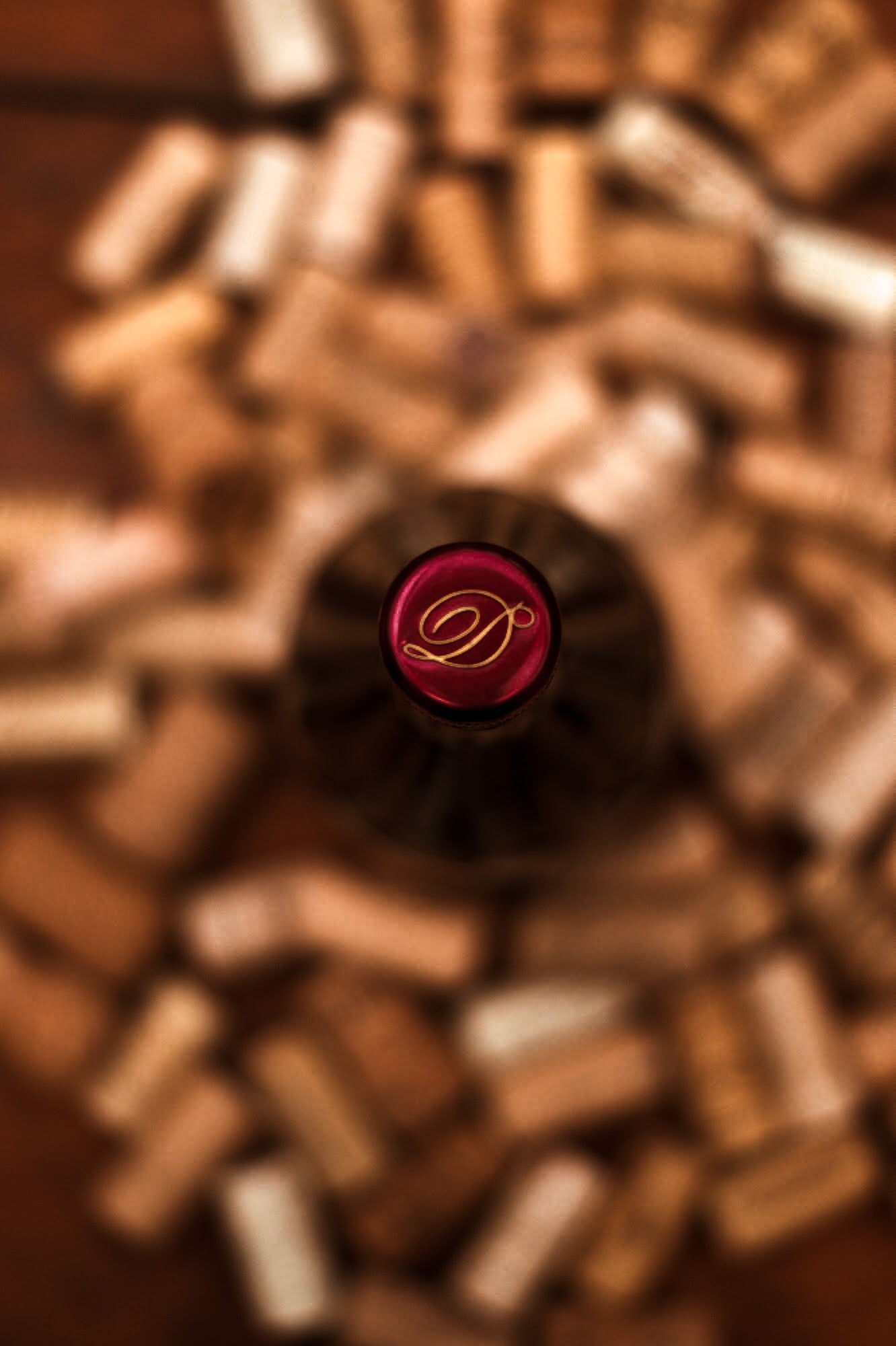 Una botella de vino tinto fotografiada desde arriba sobre un fondo de corchos de vino